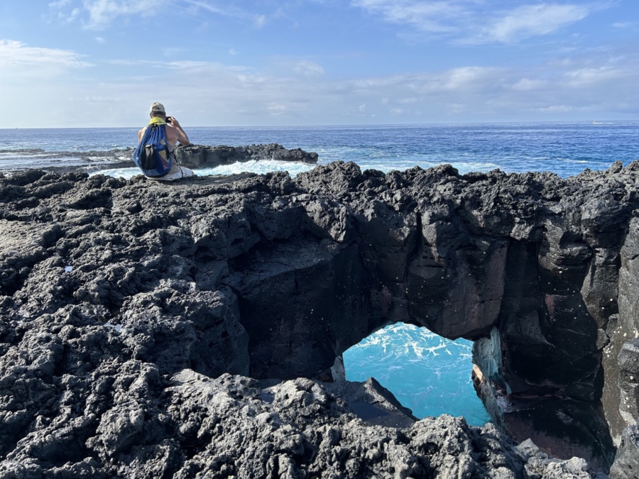 A man sitting on a stone arch above the sea